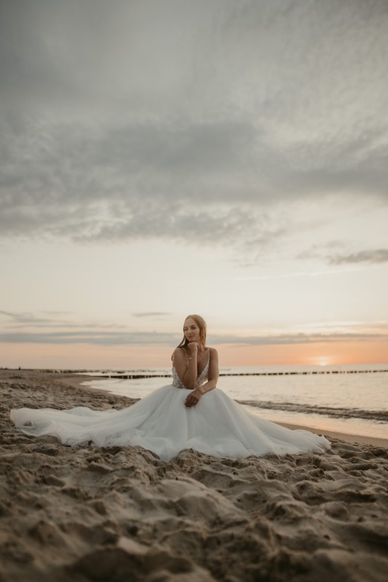 Braut sitzt im Sand bei Sonnenuntergang