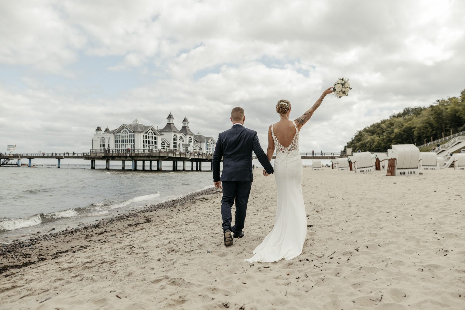 Braut jubelt mit dem Bräutigam am Strand von Sellin Richtung Seebrücke