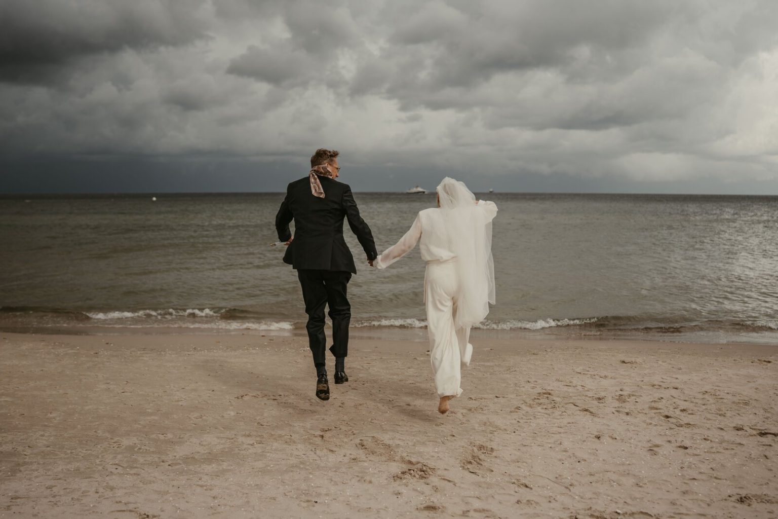 Brautpaar läuft Hand in Hand am Strand von Binz Richtung Ostsee