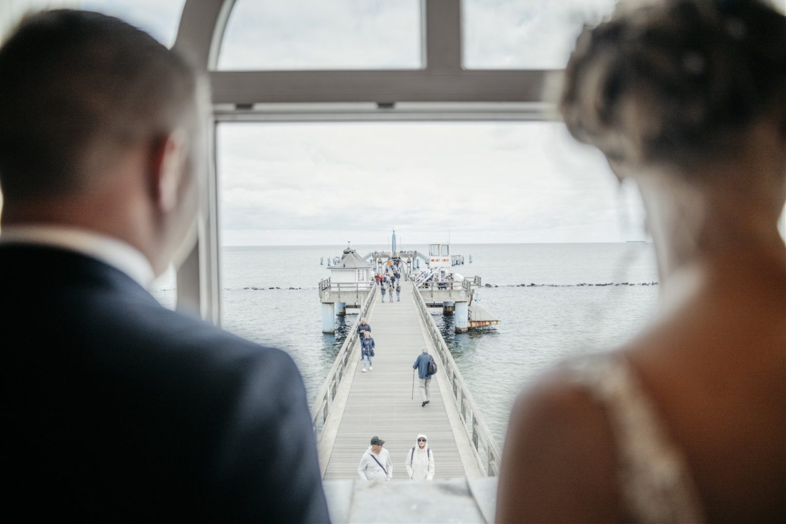 Brautpaar blickt aus dem Trausaal der Seebrücke Sellin auf den Steg und die Ostsee