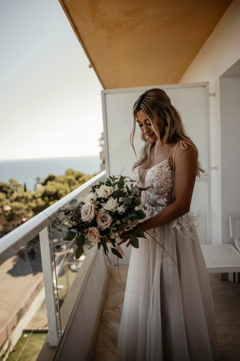 Braut Lidia mit Brautstrauß auf dem Hotelbalkon mit Meerblick auf Mallorca