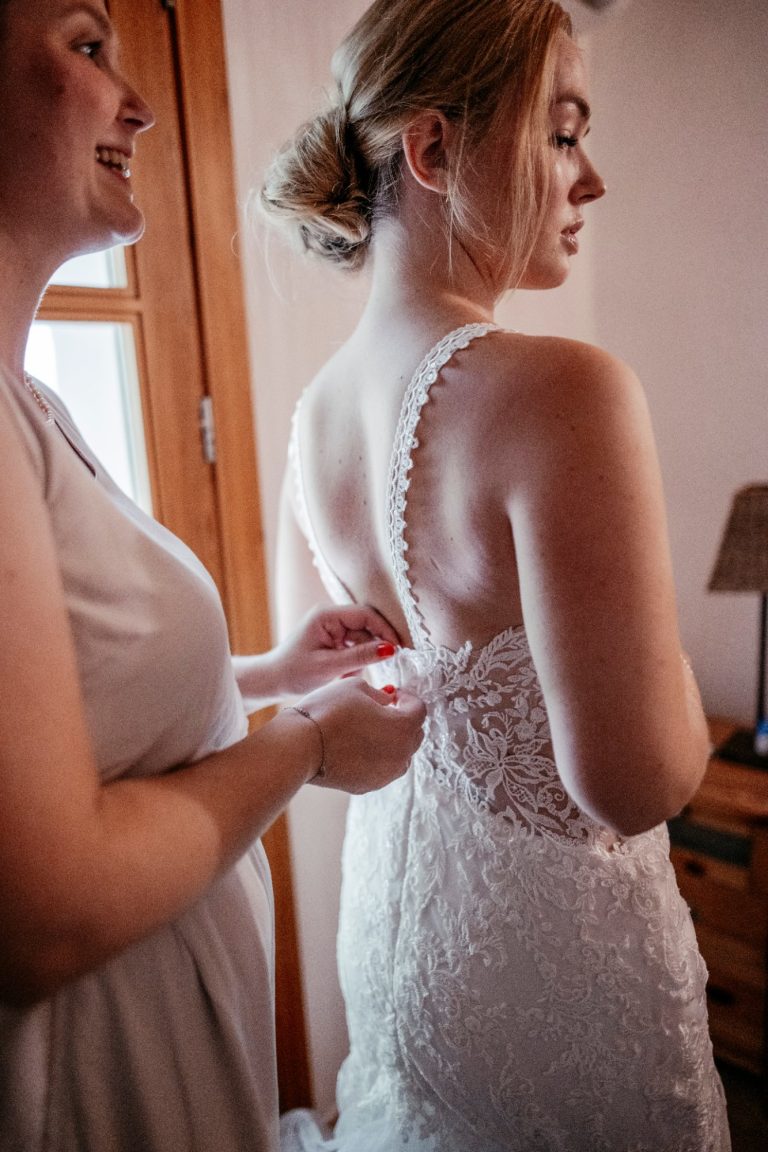 Braut wird beim Getting Ready das Kleid geschlossen